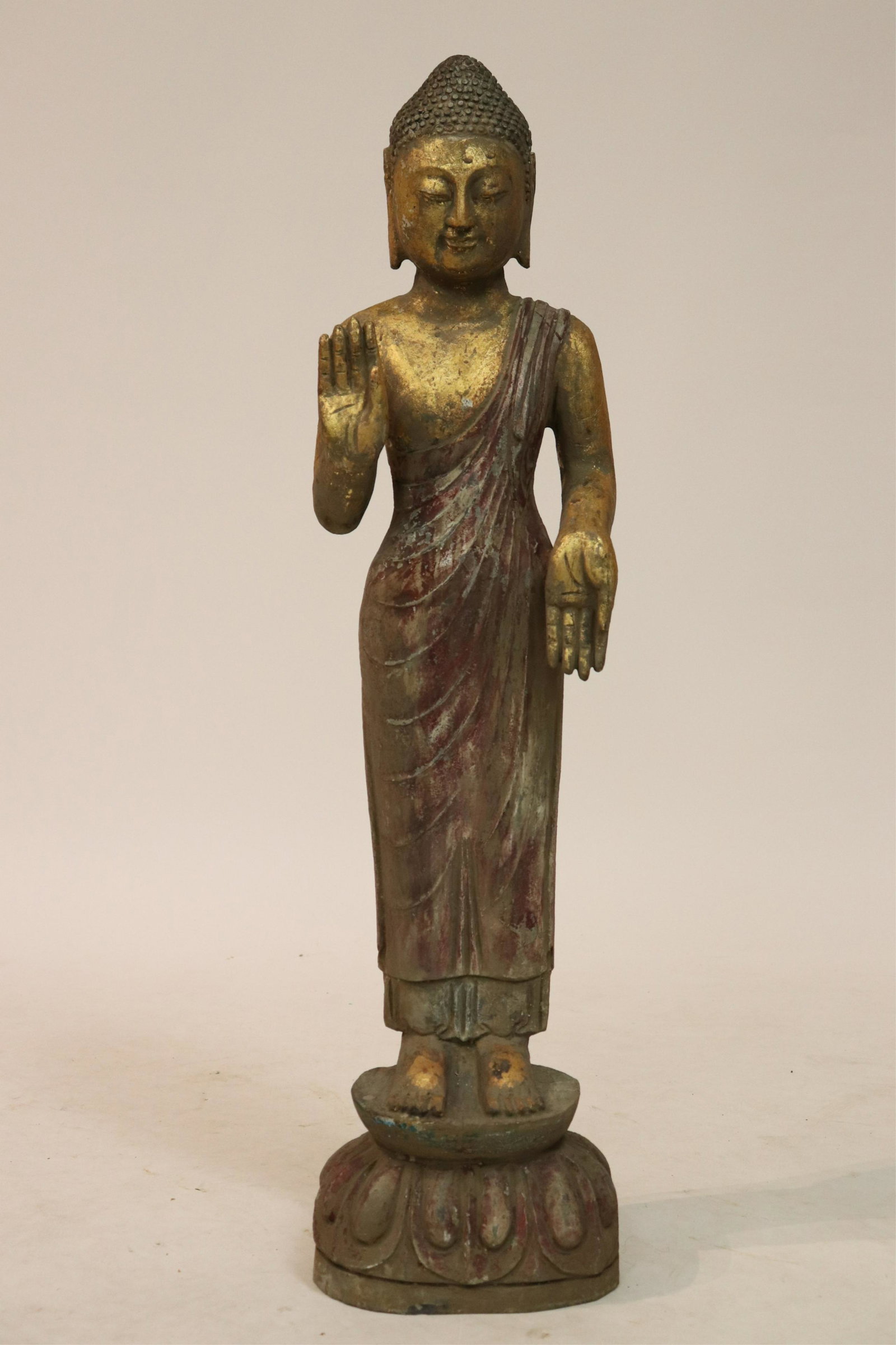 Standing Stone Buddha: Stone Buddha standing solidly on lotus plinth and in the combination of abyhaya and varada mudra. A pleasing patinal of paint and gilt applied to the surface.NOTE: This lot is being reoffered due to n