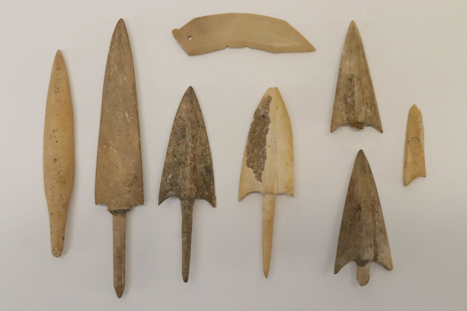 Group of Shang Dynasty Bone Arrowheads: Small Shang Dynasty Jade Blade Group of Bone Arrowheads, Shang (1766-1122 BCE) Small buff colored curved jade double-edged blade with notches and incised design near bored hole at base. Offered with s