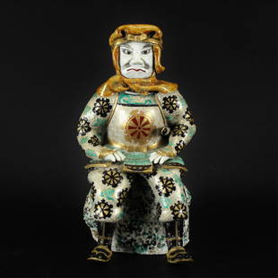 Japanese Porcelain Samurai Figure: Japanese Porcelain Samurai Figure, 20th C. Seated figure wearing cowl with tanto at side, glazed in green, black, and ochre with gilt detail accents. 12" H Property from the Estate of Marian Galewitz