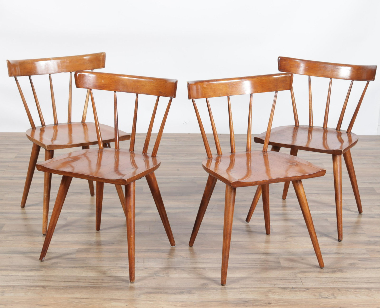 Four Paul McCobb Maple Dining Side Chairs: Chairs having shaped plank seats with visible leg through tenons and wedges, splayed and tapered legs, curved back rest on spindles. Dimensions: 20"W x 18 deep x 31H seat 17.5H