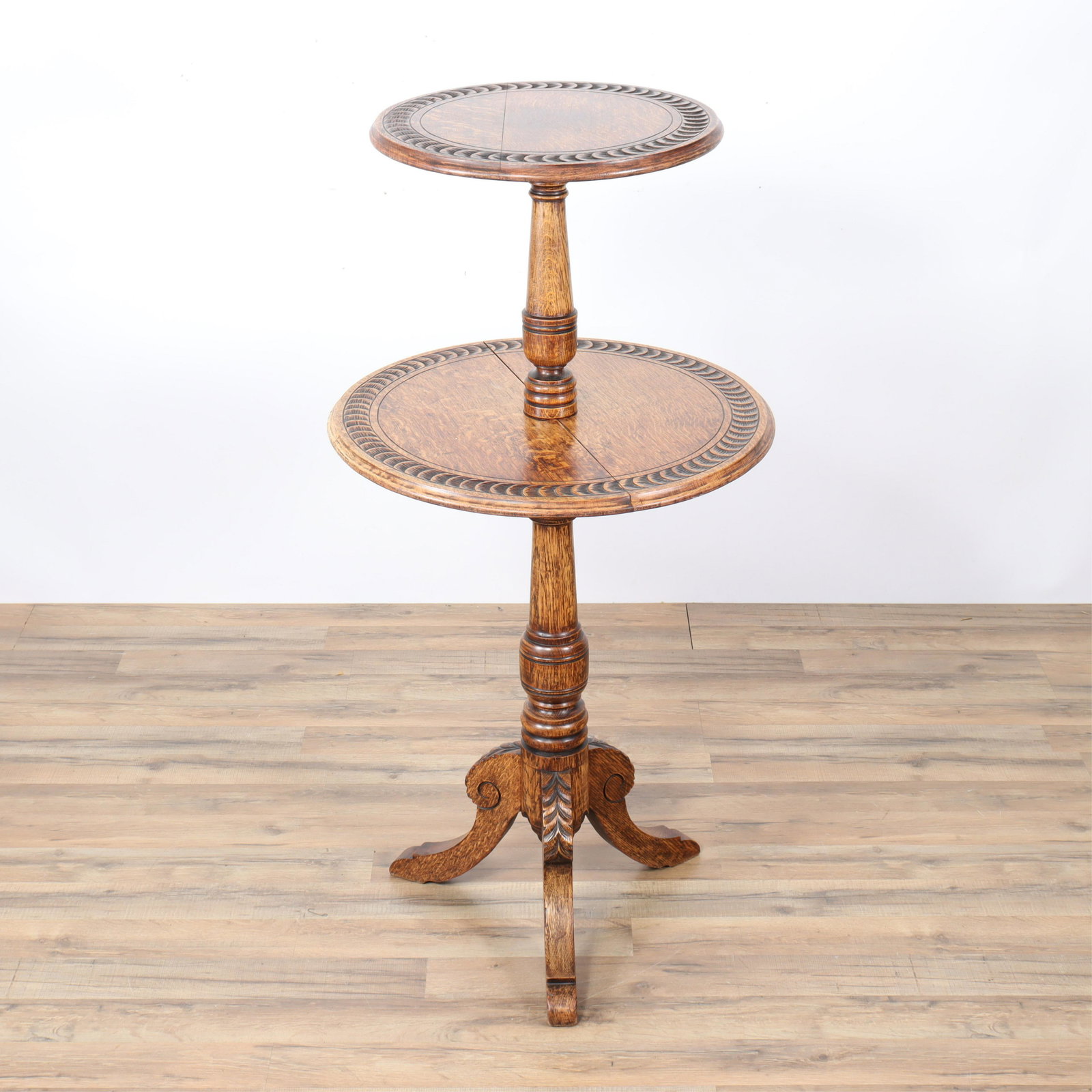 Continental Two Tier Carved Oak Dumbwaiter: Tripod base. Threaded wood dowel connection to top post and two shelves. Fish scale design carving to diameters of tops. Honey brown stained finish. Dimensions: 48"h x 24 (widest shelf) Property from 