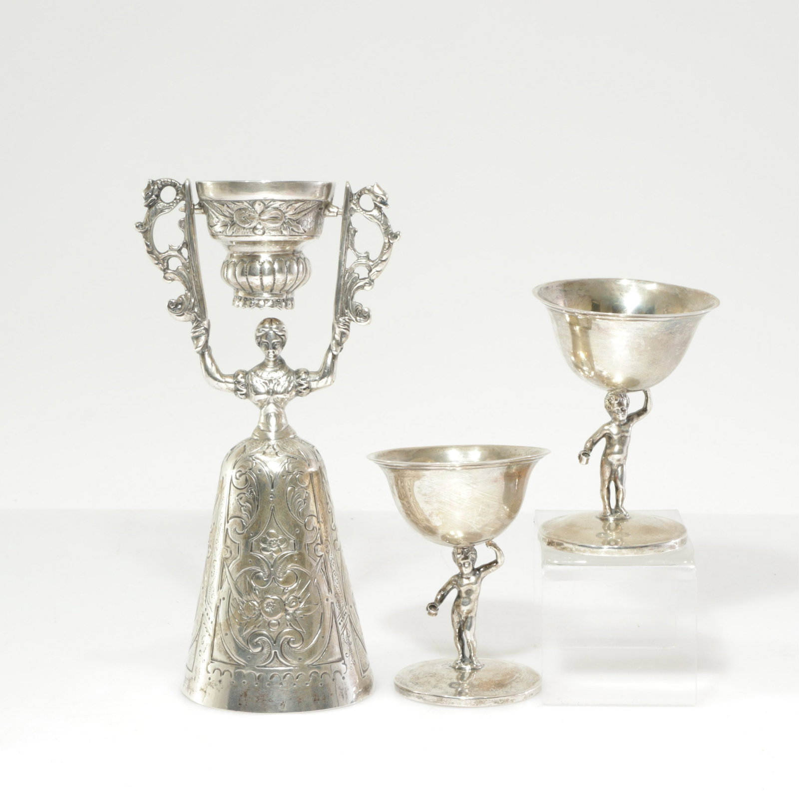 Gebruder Gutgesell Wager Cup - Putti Cordials: Gebruder Gutgesell, German, act. 1901-1925, wager cup, marked along with a pair of putti cordial cup, pseudo hallmarks possibly German Dimensions: Putti 3 1/4 x 2 1/4, Wager cup 6 3/4 x 3 3/4