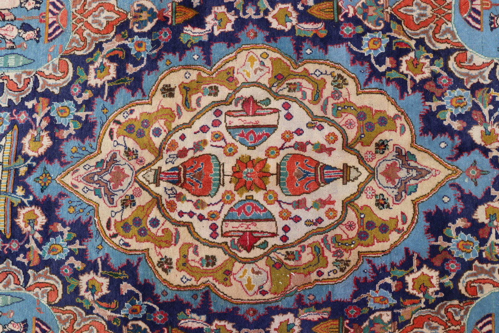 Kashmar Wool Rug 9-10 x 12-9: Pastel toned colors. Central field with water-fronted palace, figures with sunshades, urns, columns topped with animal heads and symbols. Four border bands; outside wide border with repeated deer. 9-1