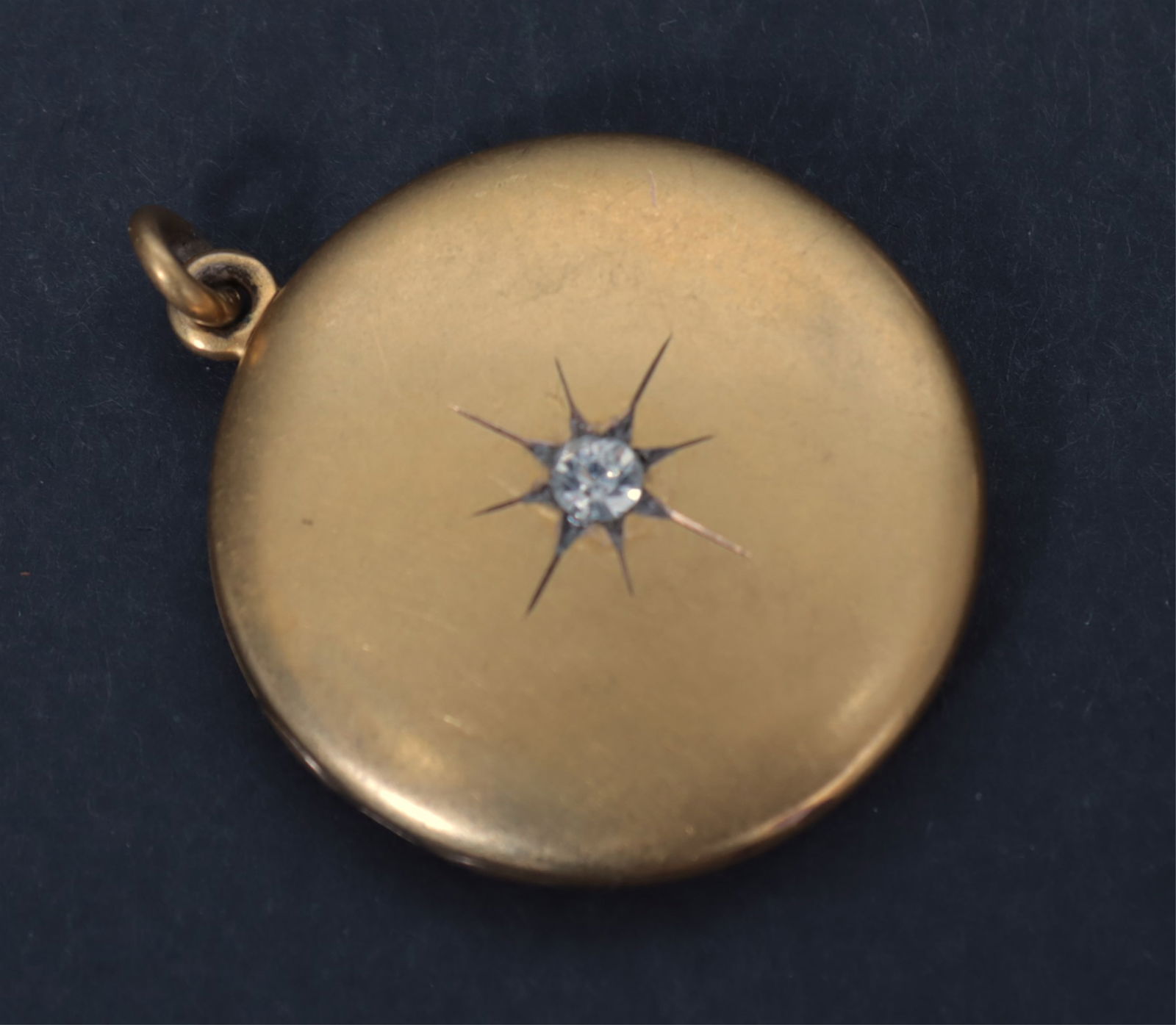 14K Gold Photo Locket Pendant: A vintage 14k yellow gold round photo locket. Interior with two photo spaces, behind plastic, framed in rose gold. Exterior with paste gemstone within starburst and monogrammed BAW verso. 7.5 grams. 1