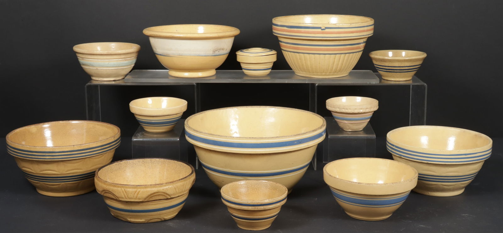 Assembled Nest of 13 Yellowware Bowls: Assembled nest of yellow-glazed earthenware bowls, with blue and pink stripes.Dimensions: Smallest: 2 1/4" H x 4" Dia; largest: 6" H x 11 3/4" Dia