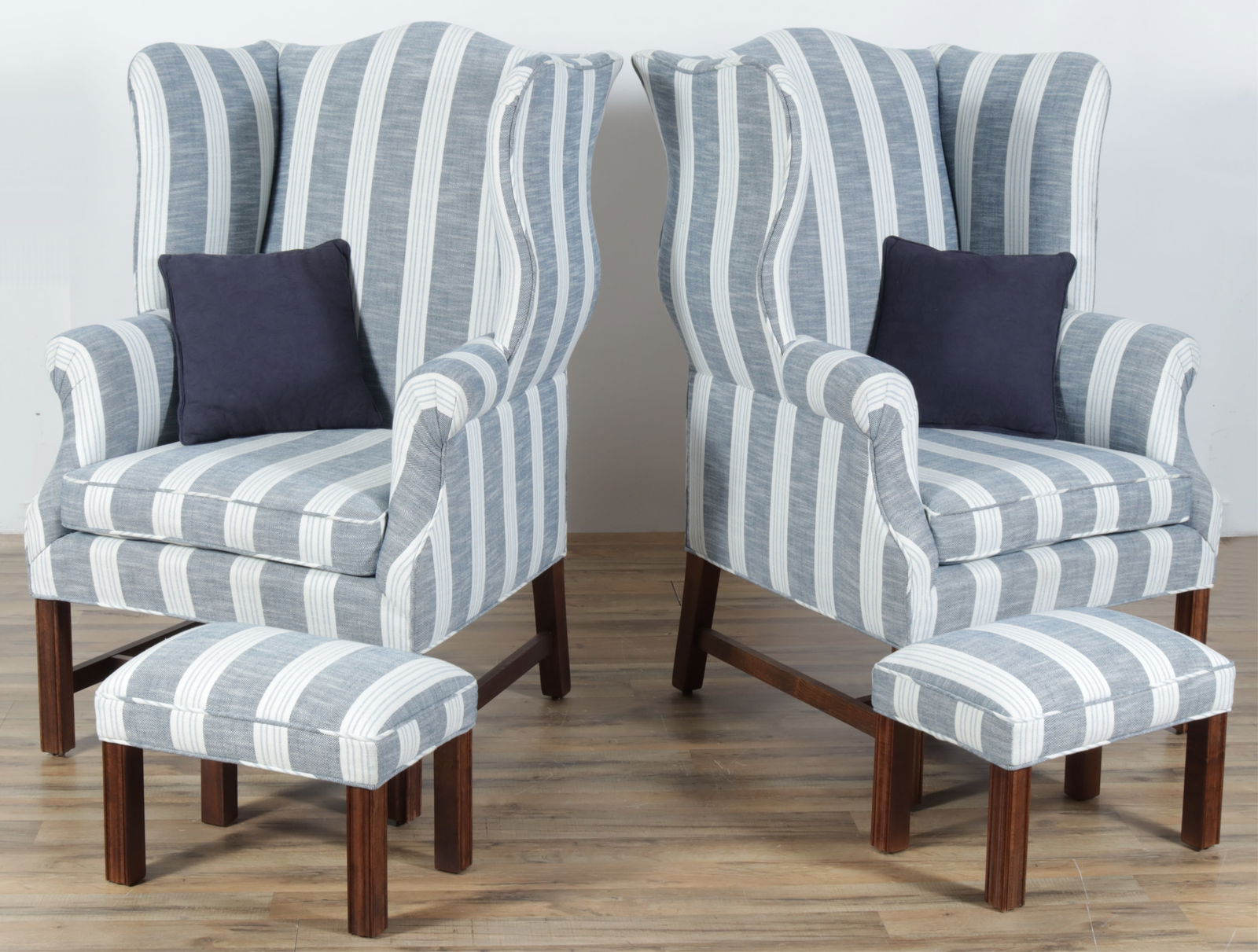 Pair George III Style Wing Chairs & Footstools: Pair of George III style mahogany wing chairs with matching foot stools and each with one blue squab cushion. Blue and white striped upholstery, molded legs, H-stretchers on chairs.Dimensions: