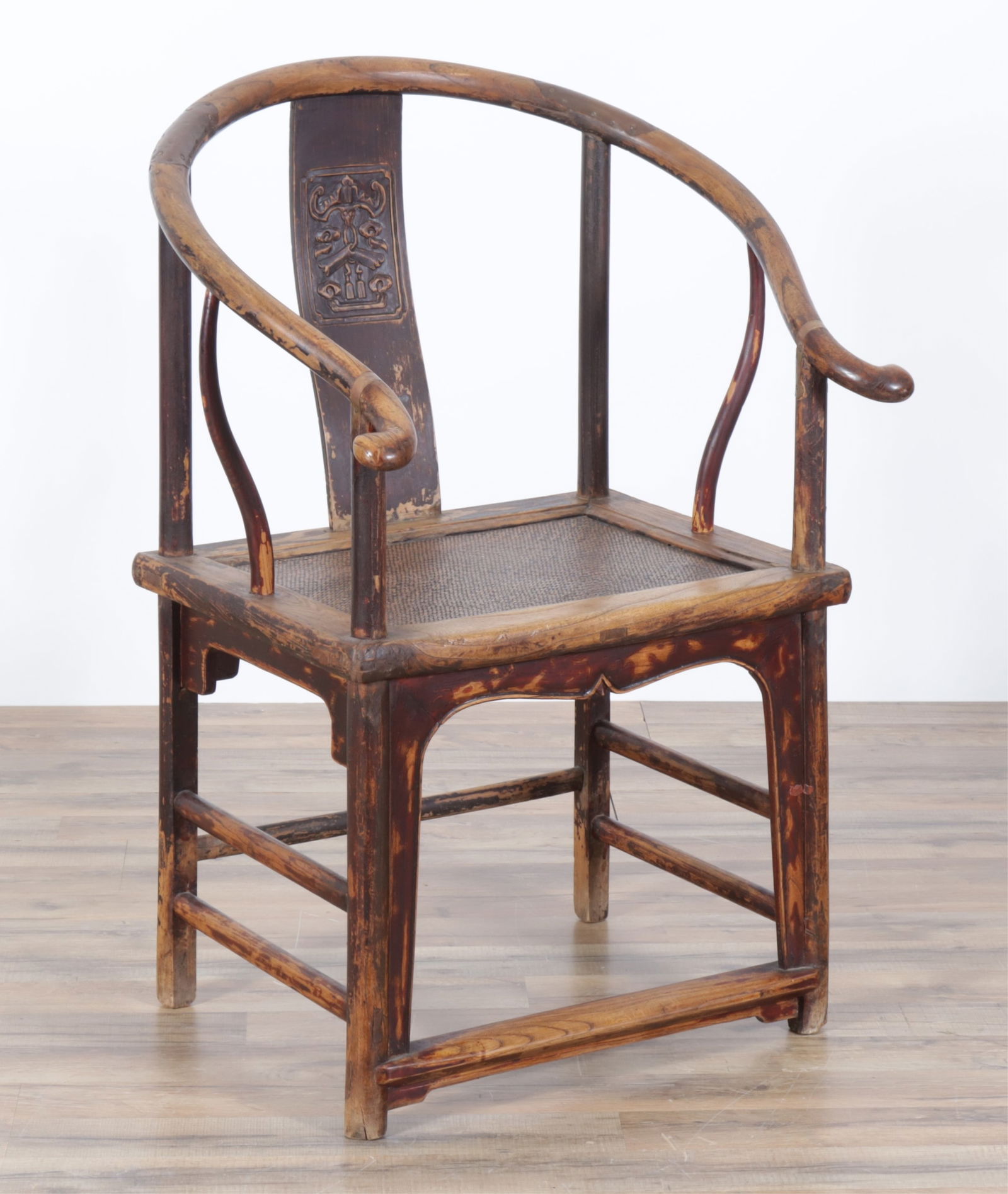 Chinese Ebonized Horseshoe Chair: Chinese carved ebonized horseshoe chair, 20th Century, rattan over plank seat, metal braces at arms and back rail, relief-carved splatDimensions: 39 1/2" H x 27" W x 25 D