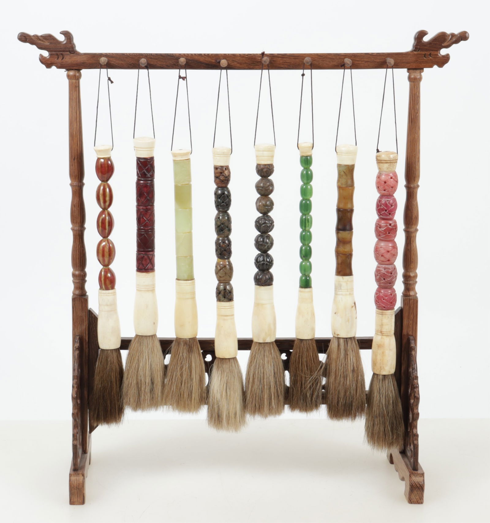 Chinese Hardstone Artist Brushes on Stand: Eight Chinese hardstone handled paint brushes on wooden stand. Dimensions: Largest brush 12.25" L