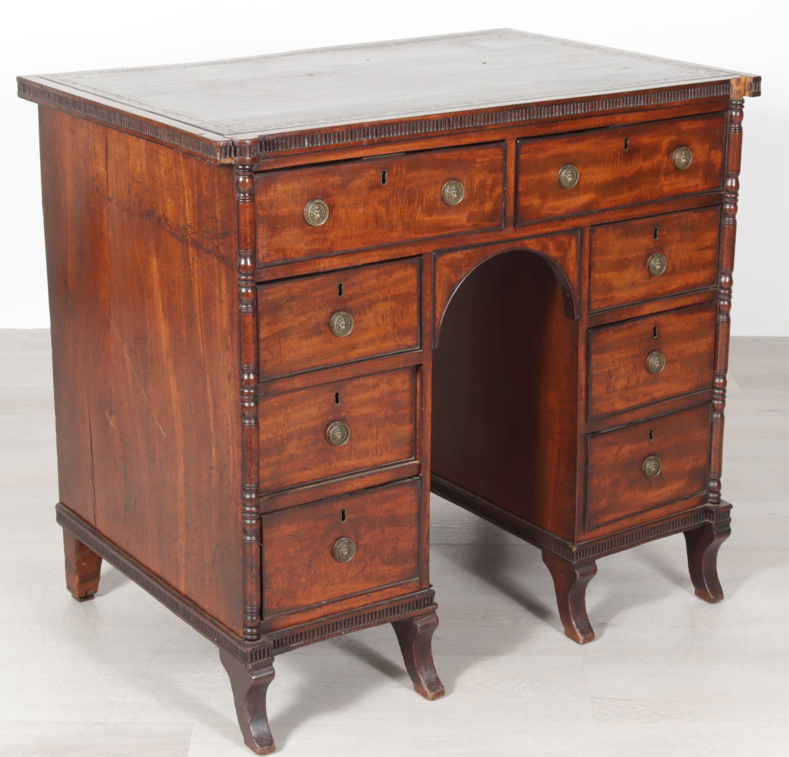 Regency Mahogany Kneehole Desk, Early 19th C.: Regency Mahogany Kneehole Desk, Early 19th C., gilt-tooled leather top above two frieze drawers over pedestals of three drawers, raised on sabre feet, with lion mask pulls. Dimensions: 35.5" H x