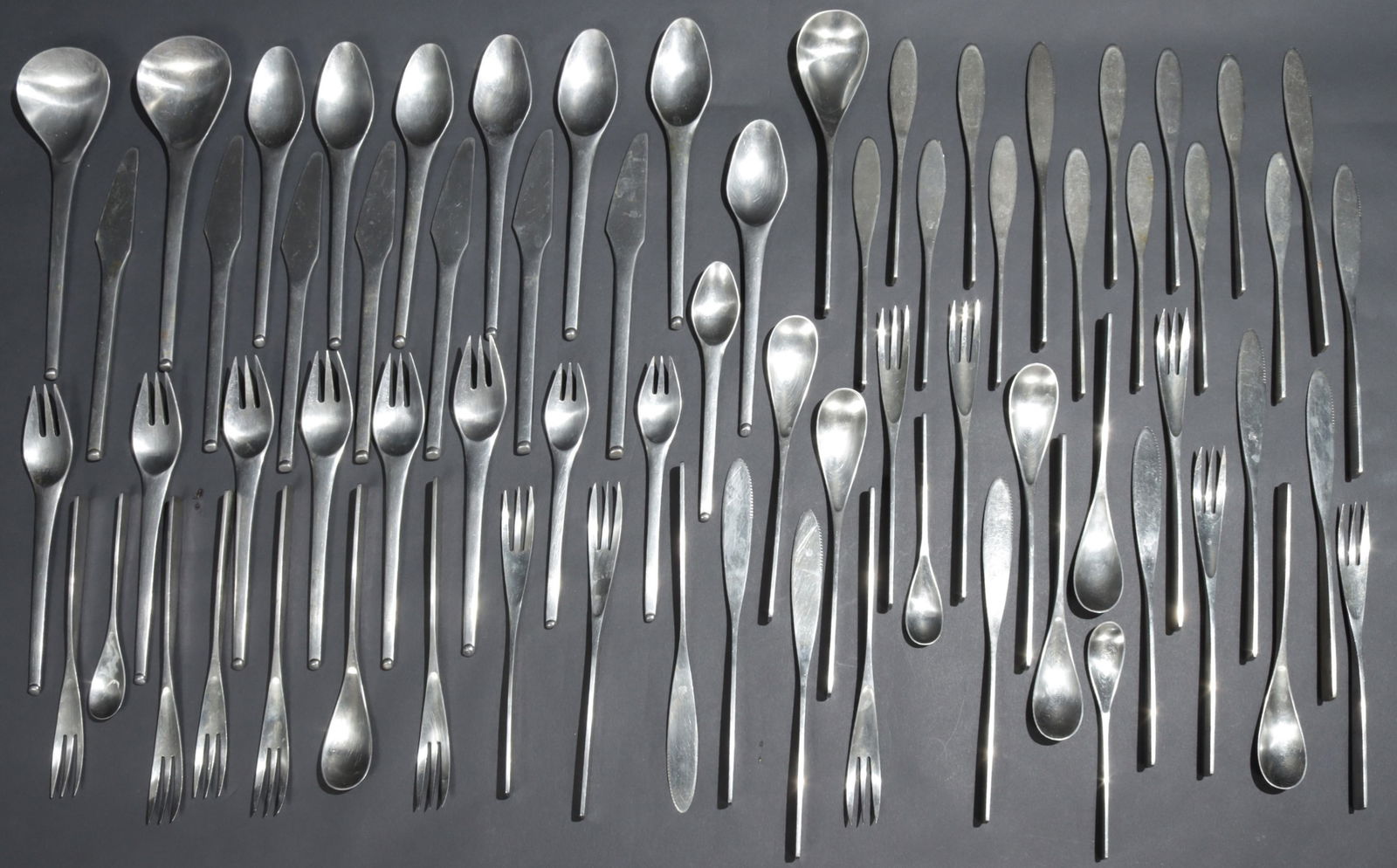 Stainless Flatware for SiVal, Stanley Roberts: Asst Midcentury Modern stainless flatware, comprising, Unique pattern by Johan Hagen for SiVal: 10 dinner knives, 7 dinner forks, 6 salad forks, 7 table spoons; 3 tea spoons, 12 butter spreaders, 1