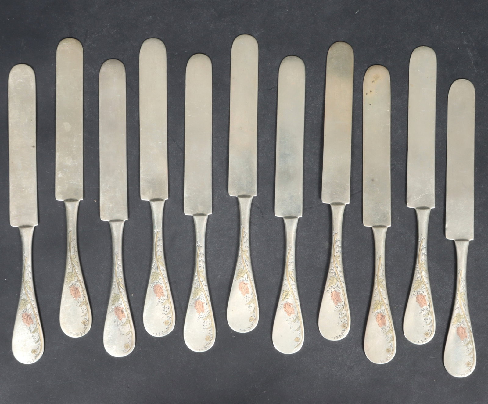 Whiting Sterling Silver Knives: A group of 11 antique Whiting Manufacturing solid handle sterling silver butter knives with incised gold, green, and rose gold butterfly and foliate design. Monogrammed M.P.W. 16.83 OZT. Dimensions: 8