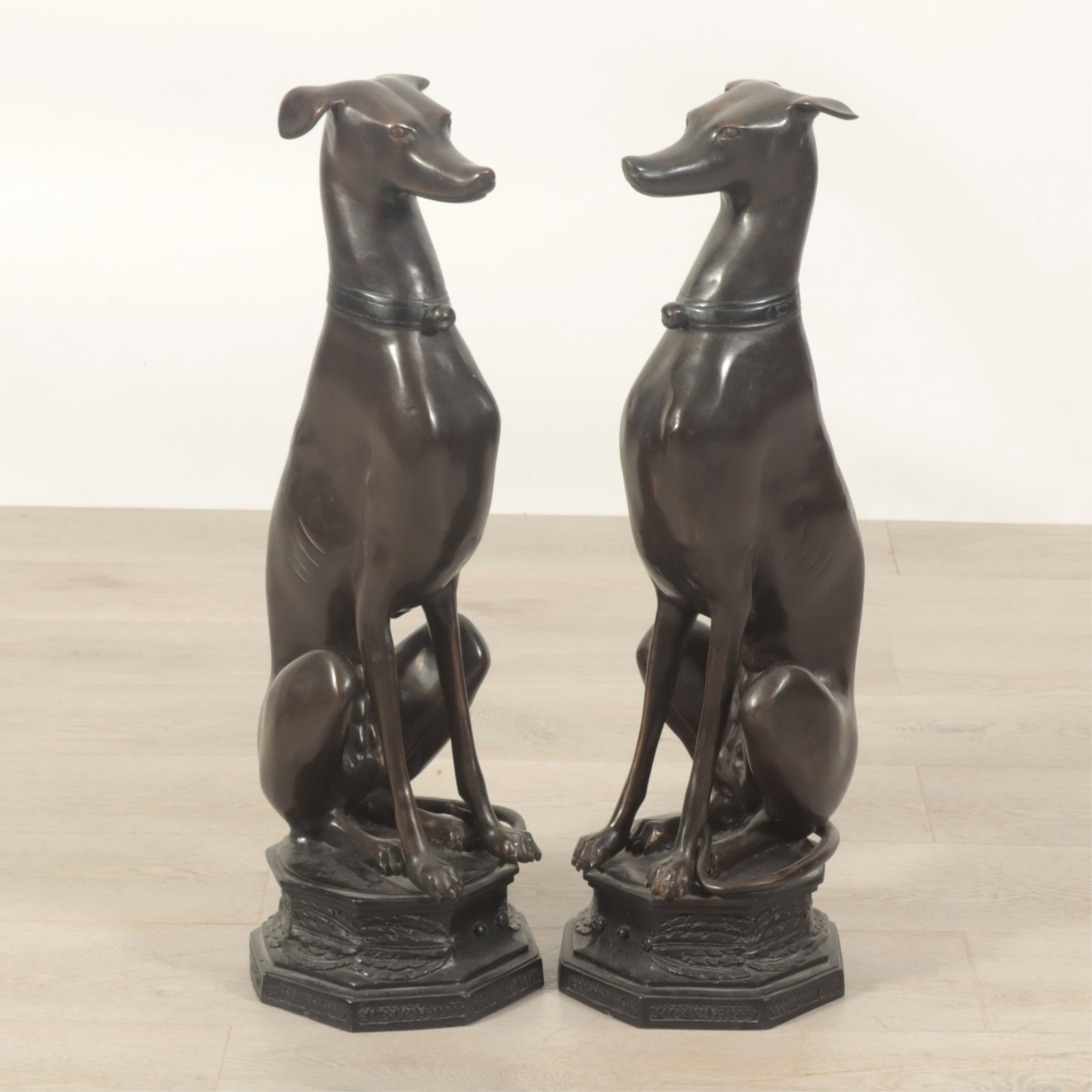Pair Bronze Seated Whippets: A pair of patinated bronze whippets seated on octagonal bases. Dimensions: 29.75" H Property from a Bronxville Estate.