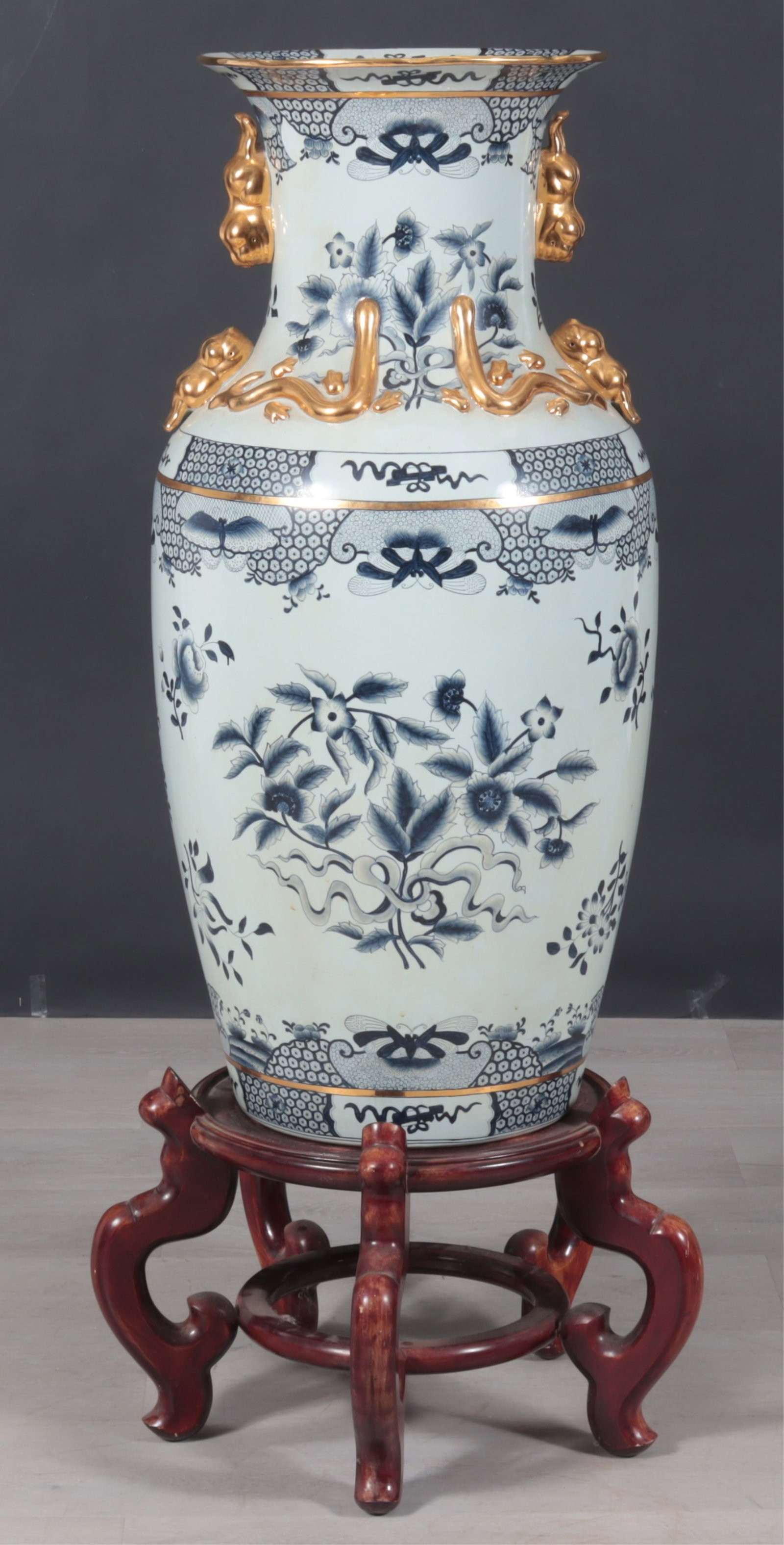Palace Size Blue & White Porcelain Vase on Stand: An ornamental size porcelain vase on hardwood stand, decorated with blue and white geometric patterns, floral sprays, and butterflies. Gilded raised relief around neck, shaped gilded rim, and figural