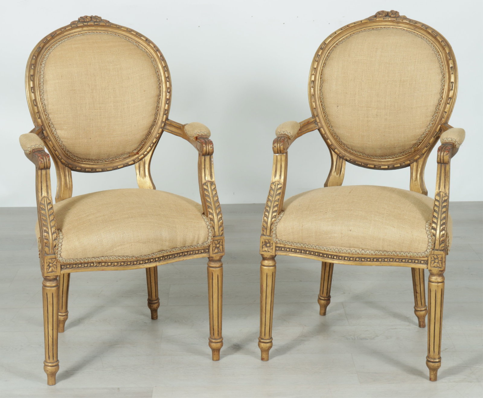 Pair Louis XVI Style Fauteuil: Pair of Louis XVI style gilt and gold paint finished fauteuil, upholstered in a woven burlap material with decorative trim, oval medallion back, carved egg and dart motif