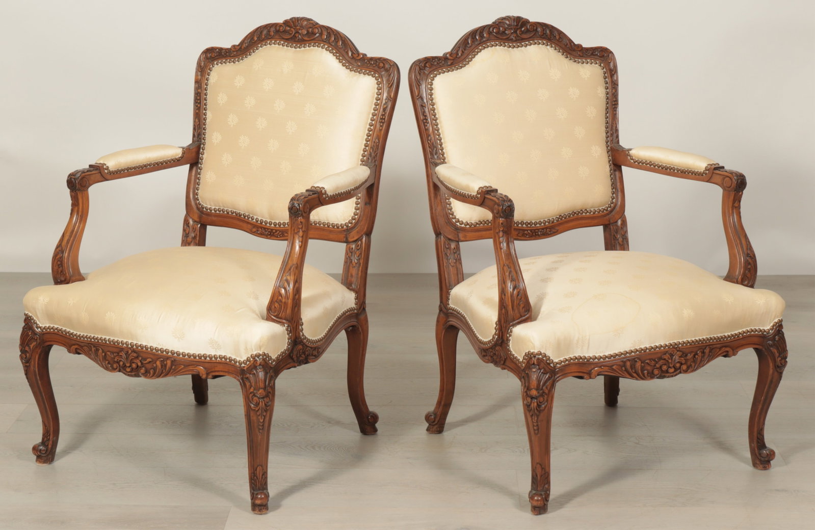 Pair of Louis XV Style Fauteuil: Pair of Louis XV style carved walnut stained fauteuil floral motif throughout, cabriole legs, cream colored fabric with sprig motif, nail head trim
