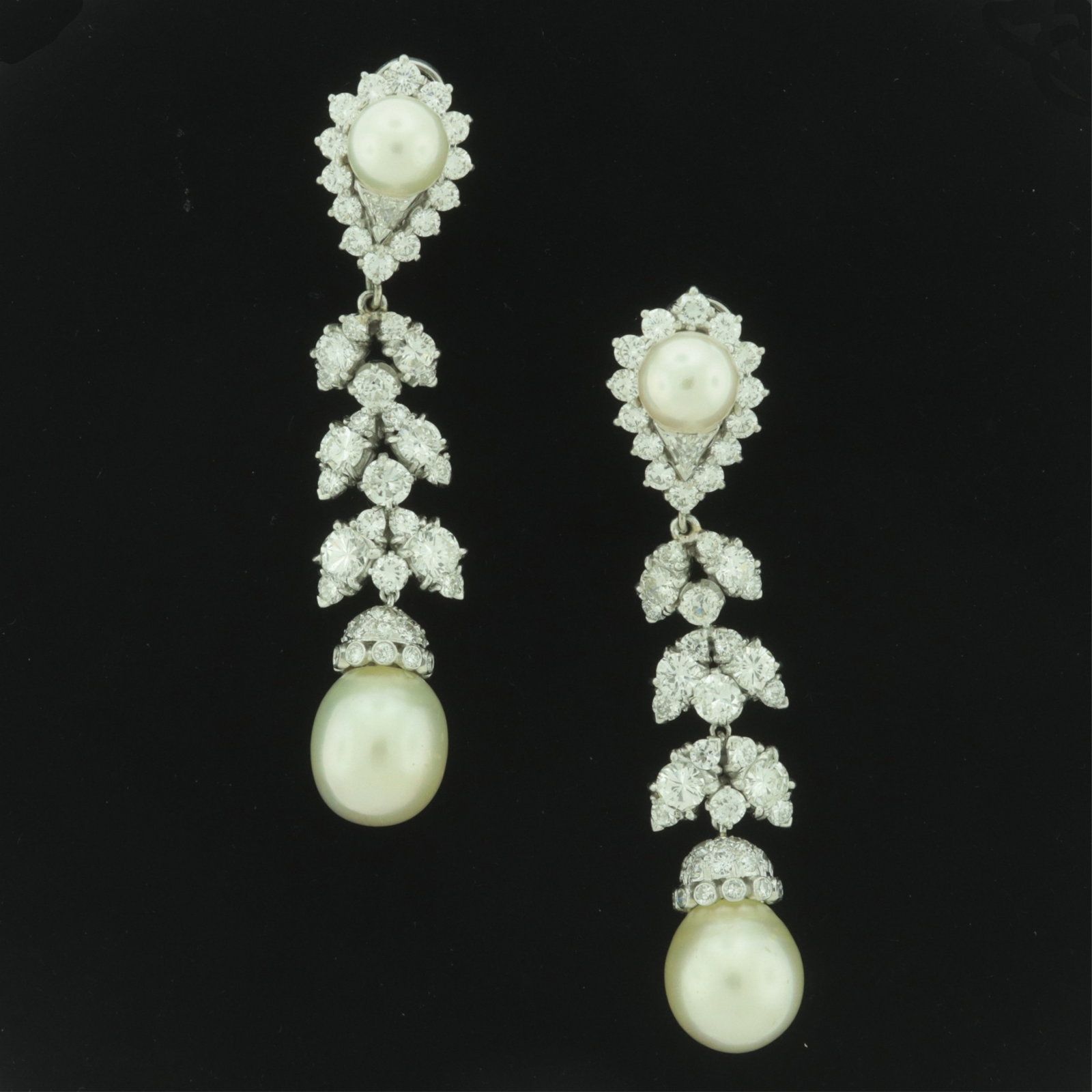 Van Cleef and Arpels Diamond & Pearl Ear Pendants: A pair of Van Cleef and Arpels diamond and cultured pearl ear pendants, circa 1970s. Cultured pearl (7.85 mm) centered surmounts with tear form halo of 14 round diamonds and one trillion cut diamond, 