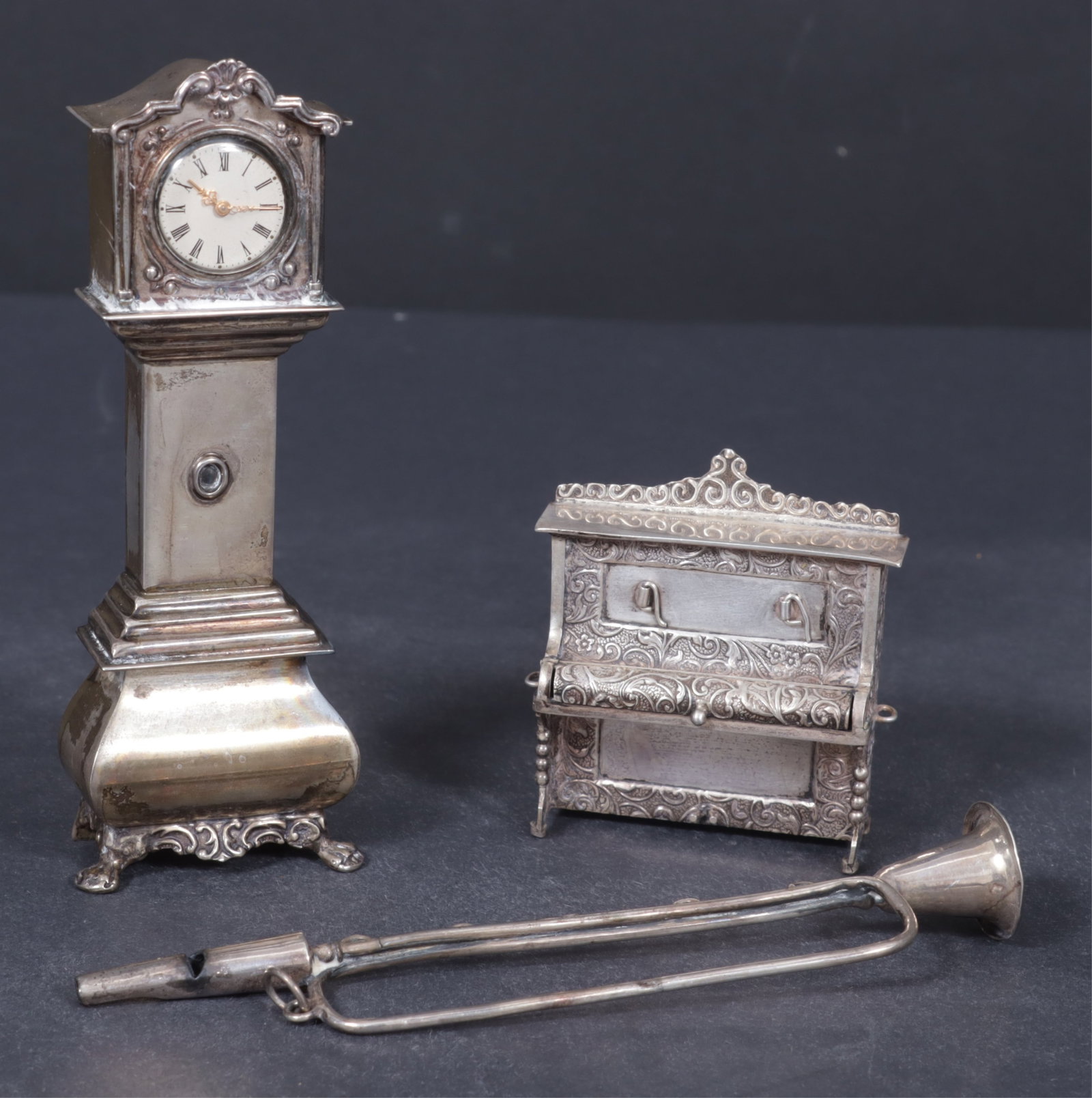 Dutch Sterling Silver Miniature Clock & Others: Two sterling silver miniatures includes a Herman Hooijkaas, Schoonhoven, Netherlands, Dutch tall case clock; a upright piano marked BT along with a whistle in the shape of a horn, total weight 4 ozt.