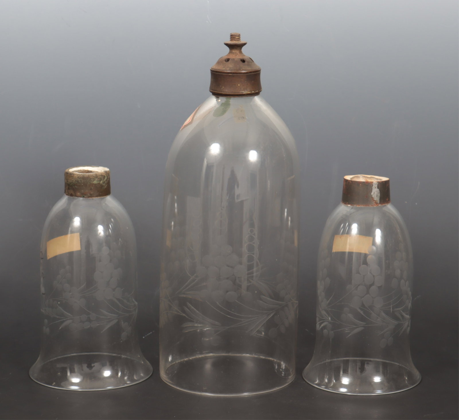 Antique Etched Glass Hurricane Shades: A grouping of three antique glass hurricane shades with etched floral and vine motif. A pair of bell form, together with a single. 7.75" H x 4.75" bottom diameter. 13.25" H x 5.25" bottom diameter.