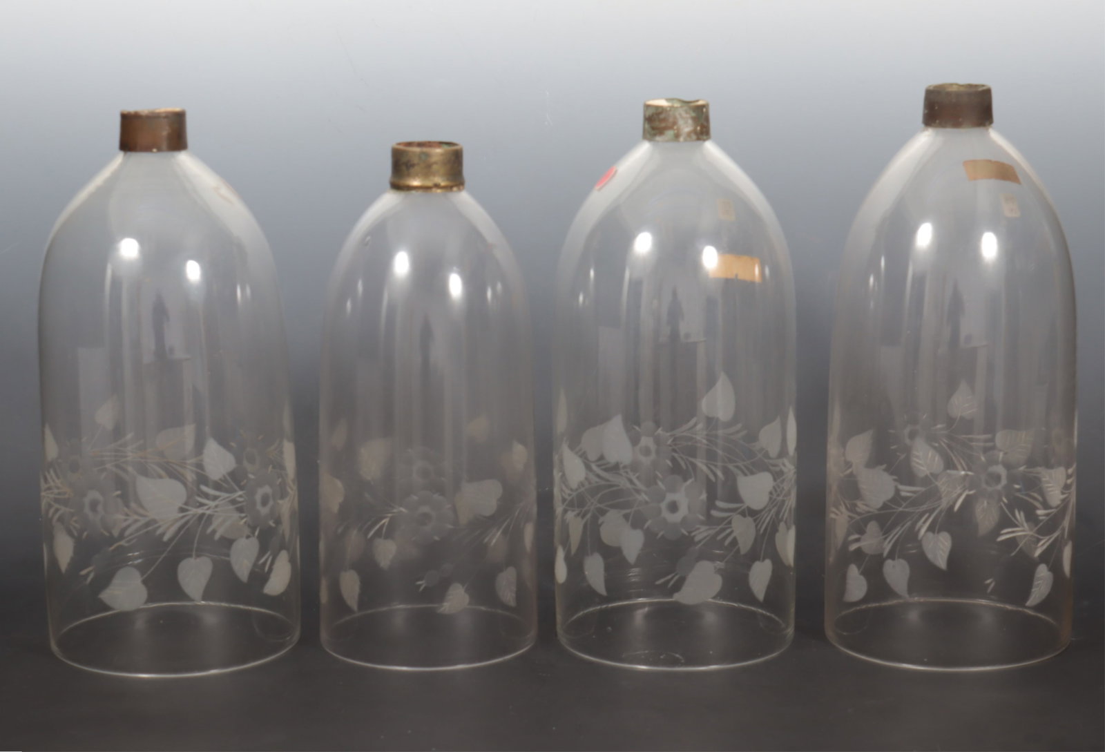 Four Antique Glass Hurricane Shades: A group of four antique glass hurricane shades with etched floral and vine motif. Comprising: three of very similar size and one single smaller. 14 1/2" H x 6 1/2" bottom diameter. 13 3/8" H x 5 3/4" 