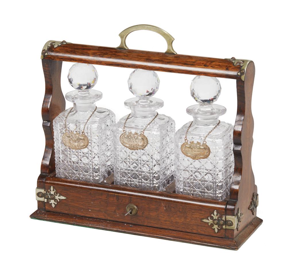 Victorian Tantalus: Victorian oak tantalus with brass mounts containing three stopped bottles. Lockable with key. Overall dimensions: 13.5"h x 14.5"w. Provenance: Estate of Wm. B. Ruger, Jr. Processing and shipping withi