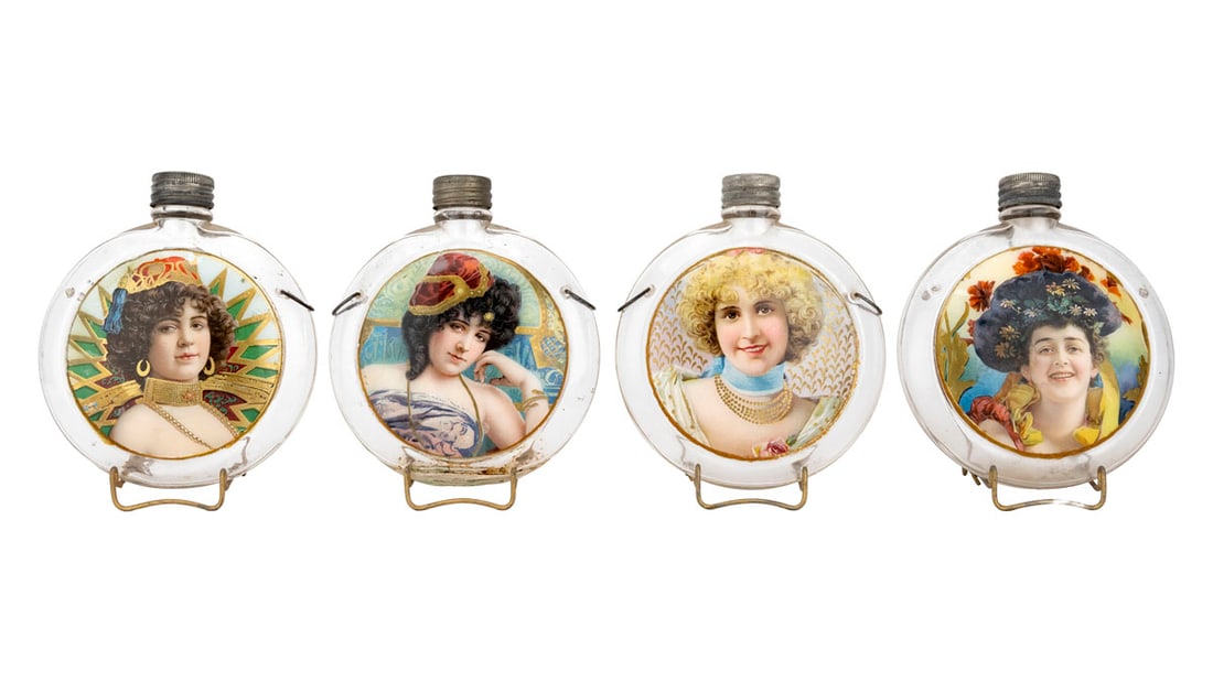 Four Label-Under-Glass "Pretty Lady" Canteen-Form Whiskey Bottles, ca. Early 20th Century: A scarce group of four circular clear glass canteen-form whiskey bottles featuring vibrant label-under-glass portraits of idealized women, each with vivid color palettes and stylized backgrounds. The