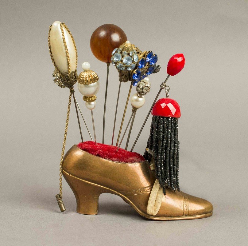 Victorian Hatpins in Vintage "Pin Cushion" Shoe: Victorian Hatpins in Vintage "Pin Cushion" Shoe. Approximately 9 hatpins with colored stones, rhinestones and gold filigree in a brass/copper shoe. Dark blue rhinestone hatpin has a matching 3-stone 