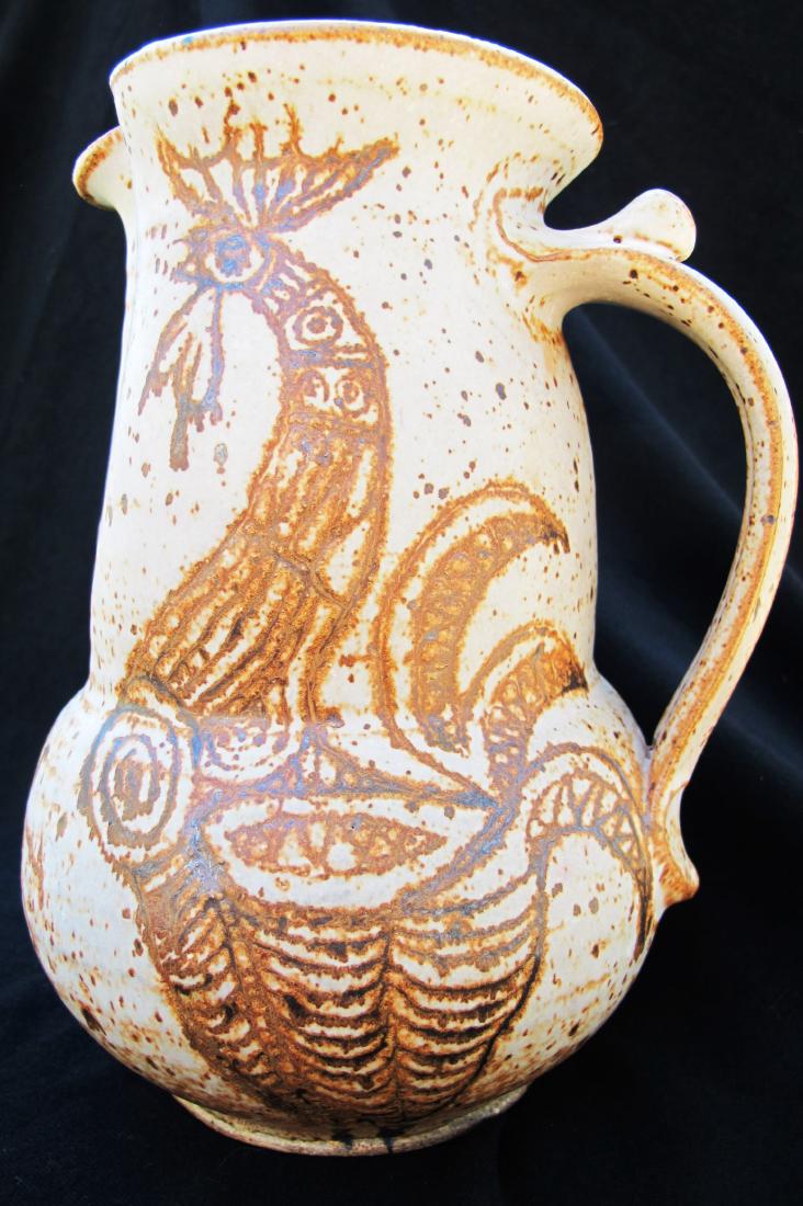 rooster pitcher: This beautiful stoneware pitcher by artist Angelo Garzio features two roosters on either side. The text at the front of the pitcher states "Garzio did this." It is a full-sized pitcher in good conditi