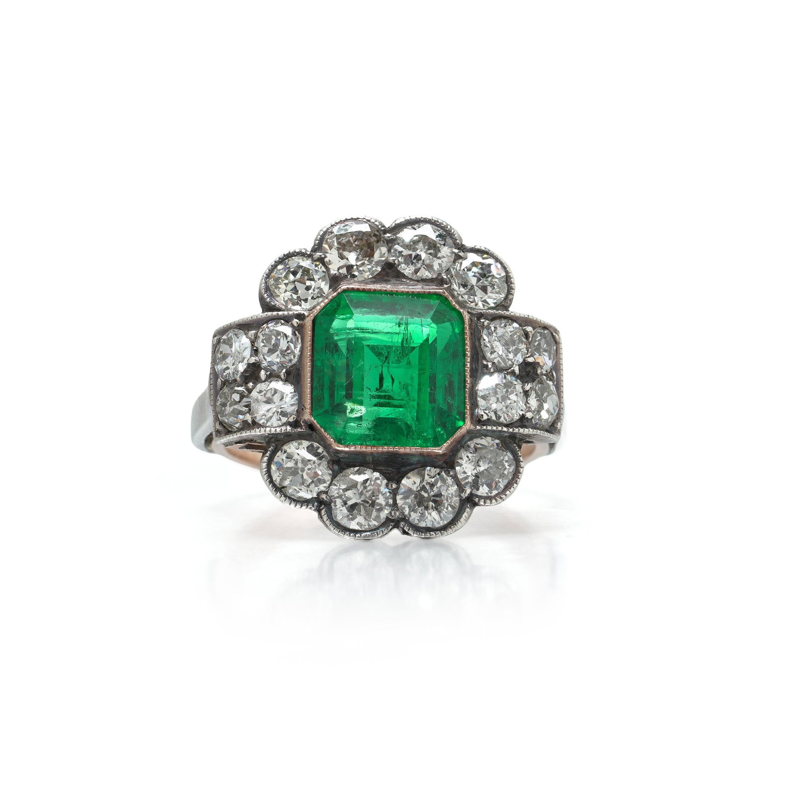Victorian Colombian Emerald and Diamond Cluster Ring, 9KT Gold and Silver: Victorian Colombian emerald and diamond cluster ring, the emerald cut centre stone framed by a scalloped border of old European cut diamonds, in silver settings over a 9KT gold shank. The emerald is r