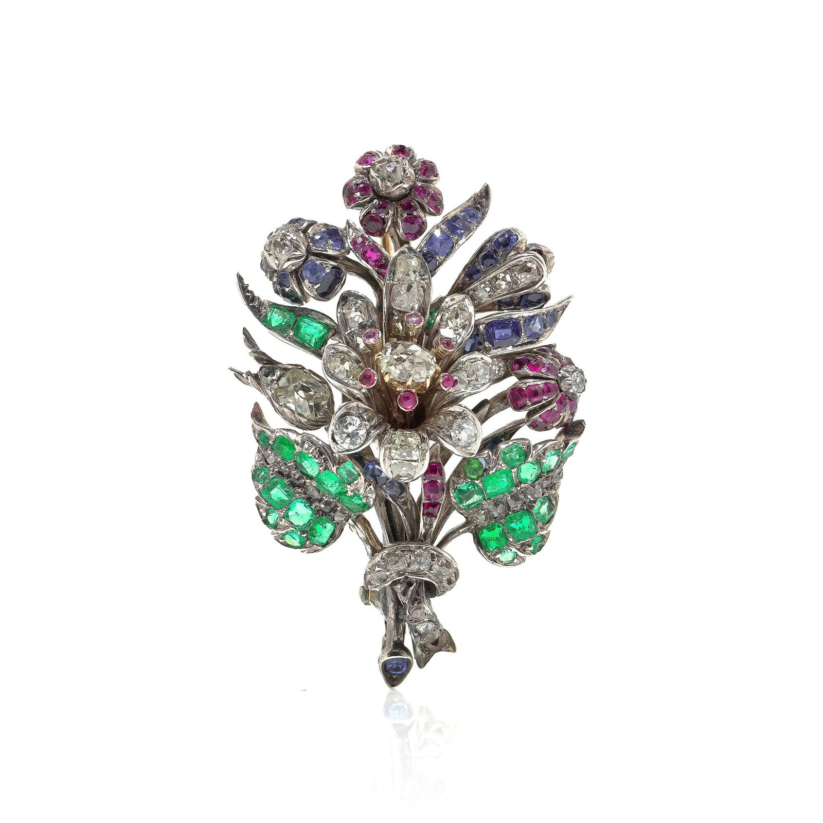 Victorian 9KT Gold and Silver Emerald, Ruby, Sapphire and Diamond Floral Brooch: A Victorian floral brooch in 9KT gold and silver, dating to the 1890s, designed as a naturalistic flower spray set with emeralds, rubies, sapphires, and diamonds. The brooch is arranged as a richly de