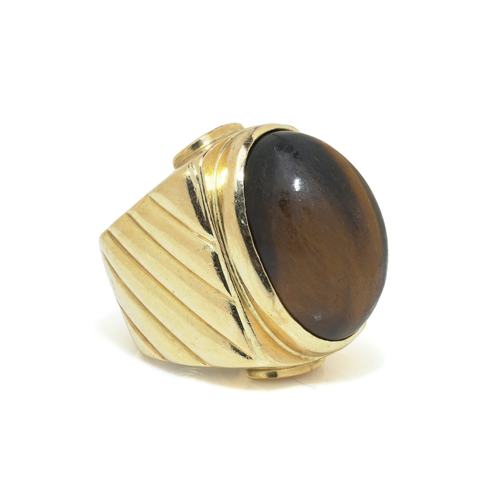 Vintage 1970s 18KT Gold Tiger's Eye Ring: A vintage 1970s ring crafted in 18KT gold and set with a large oval tiger's eye cabochon. The mount is bold and sculptural, with fluted diagonal ridges to the shoulders and a heavy overall form typica