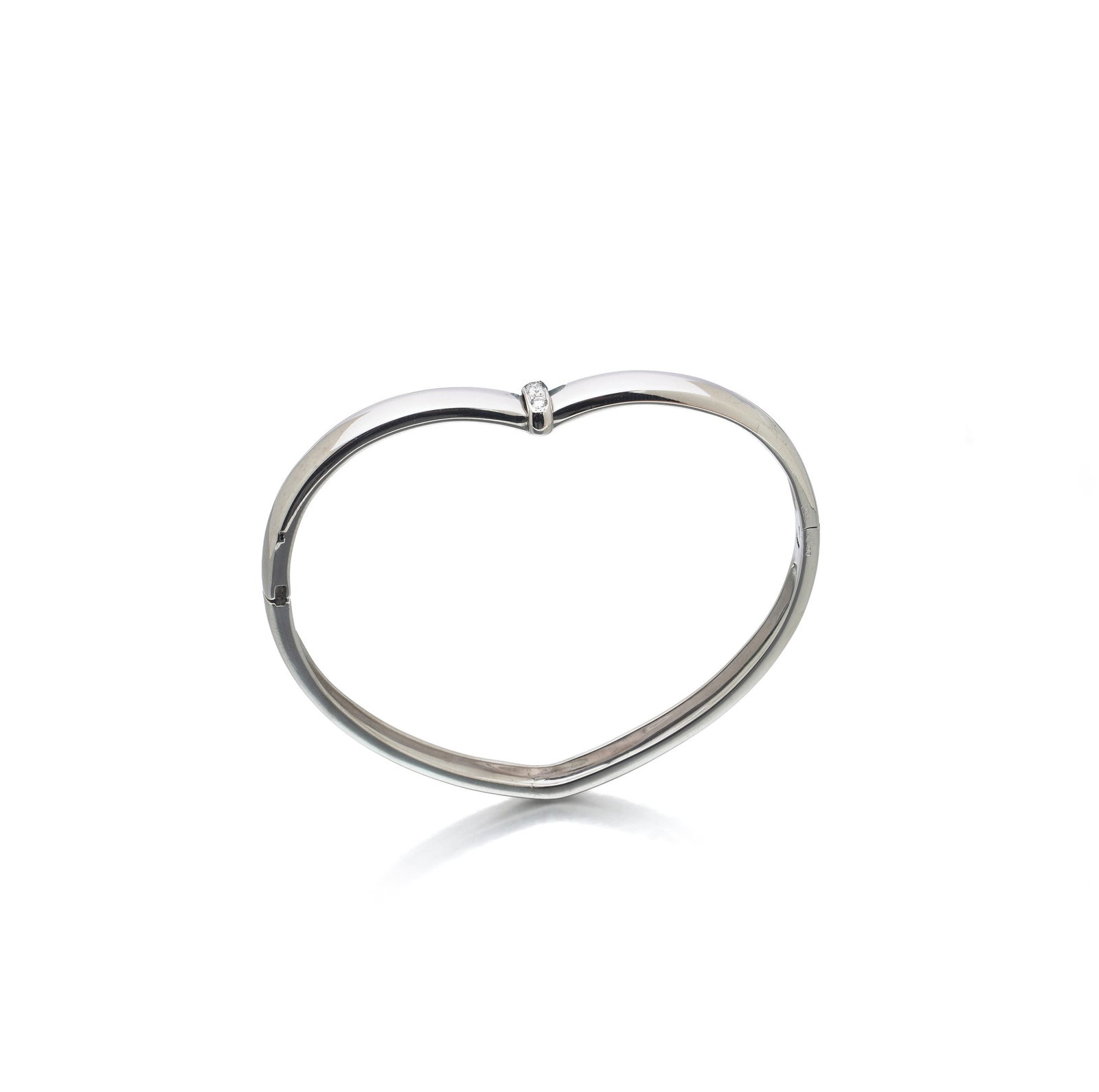 Piaget 18KT White Gold Diamond Heart Bangle, 1997: Piaget heart bangle in 18KT white gold, the polished band drawn into a heart when seen from above, with a diamond collet set at the cleft. The bangle is hinged and closes with a concealed box clasp an