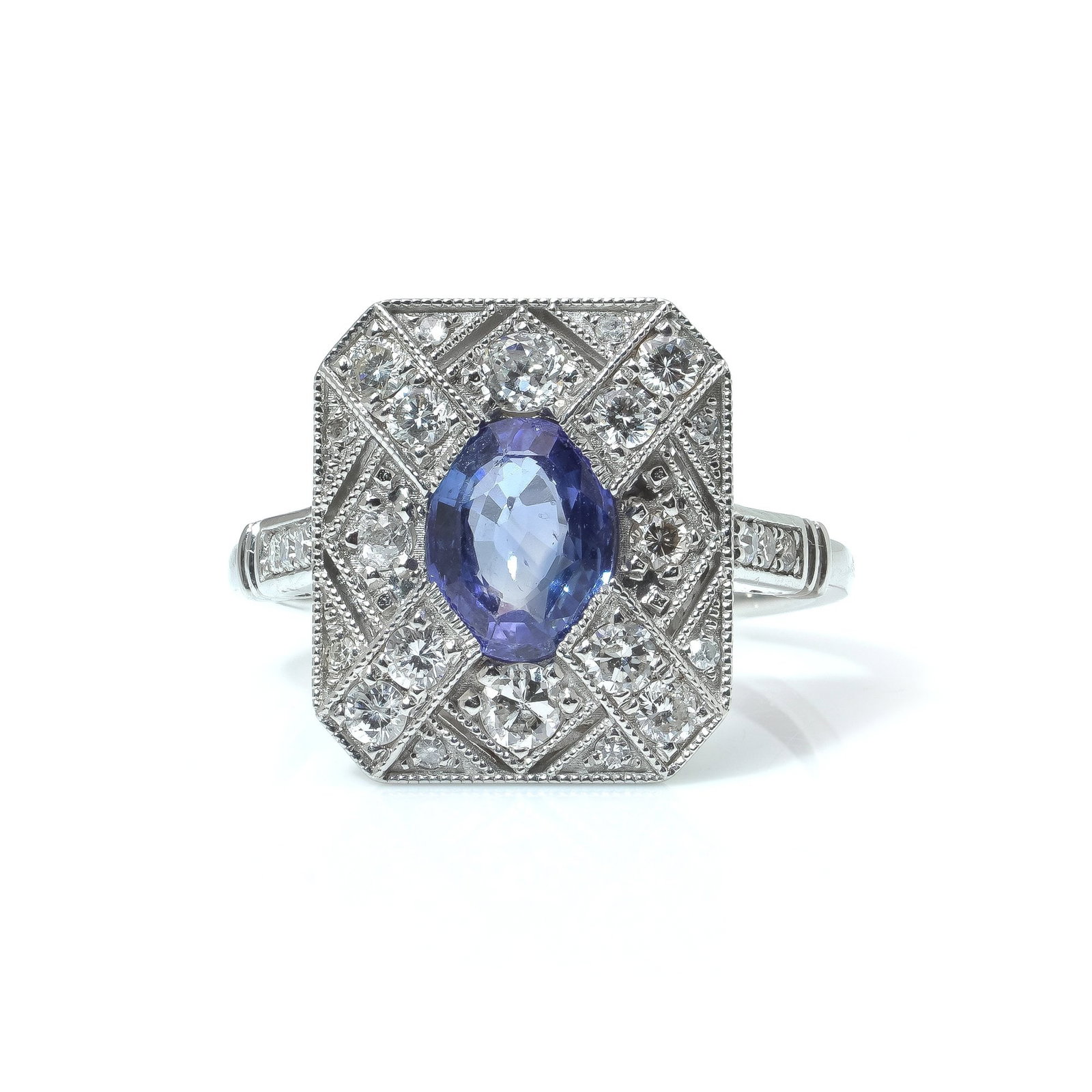 Art Deco Style Sapphire and Diamond Ring: A modern Art Deco style ring centred with an oval-cut sapphire, set within a geometric octagonal plaque highlighted by diamond-set panels and fine millegrain detailing. The layout gives the piece a cr