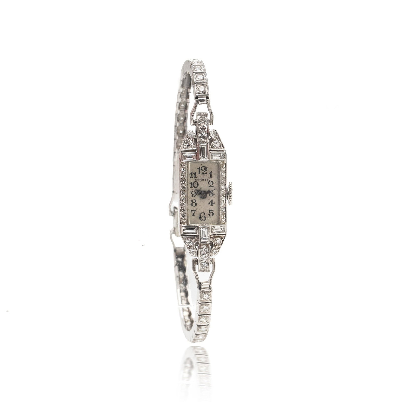 Tiffany & Co. Art Deco Platinum Diamond Cocktail Watch, Circa 1938: A late Art Deco ladies cocktail watch by Tiffany & Co., circa 1938, the slender rectangular platinum case framed by geometric diamond borders and stepped architectural shoulders, running into a fully 