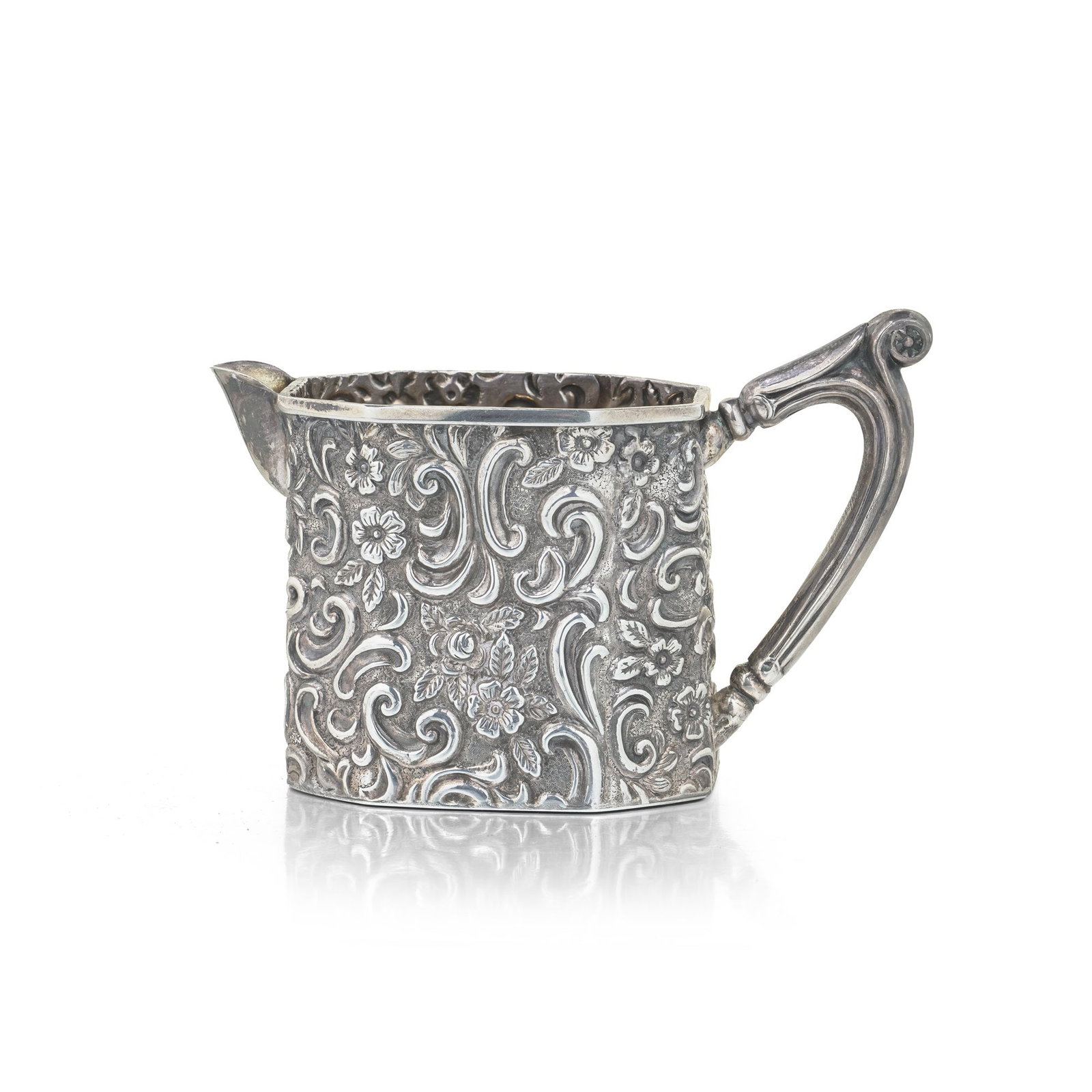 Victorian Sterling Silver Embossed Cream Jug, Birmingham 1897: A small Victorian sterling silver cream jug, fully hallmarked for Birmingham in 1897. Despite its diminutive size, the jug is richly worked in high-relief repousse and chasing, with scrolling foliage,