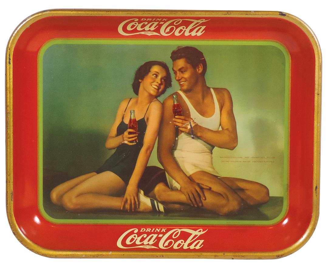 Coca-Cola serving tray, 1934, Maureen O'Sullivan &: Coca-Cola serving tray, 1934, Maureen O'Sullivan & Johnny Weissmuller, litho on metal by The American Art Works, VG+ cond w/some loss on Johnny's hand, Exc color & gloss, 10.5"H x 13.25"W.