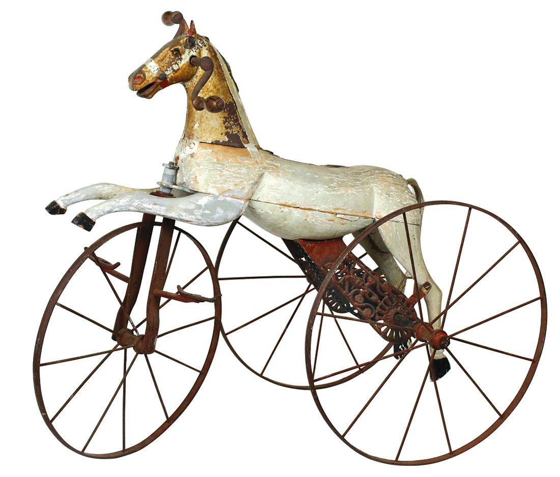 Toy Horse Velocipede, French, circa 1870, carved &: Toy Horse Velocipede, French, circa 1870, carved & polychrome wood w/cast iron head, glass eyes & wire spoke steel wheels w/chain drive, Good cond w/replaced leg, losses to paint, saddle & mane absent