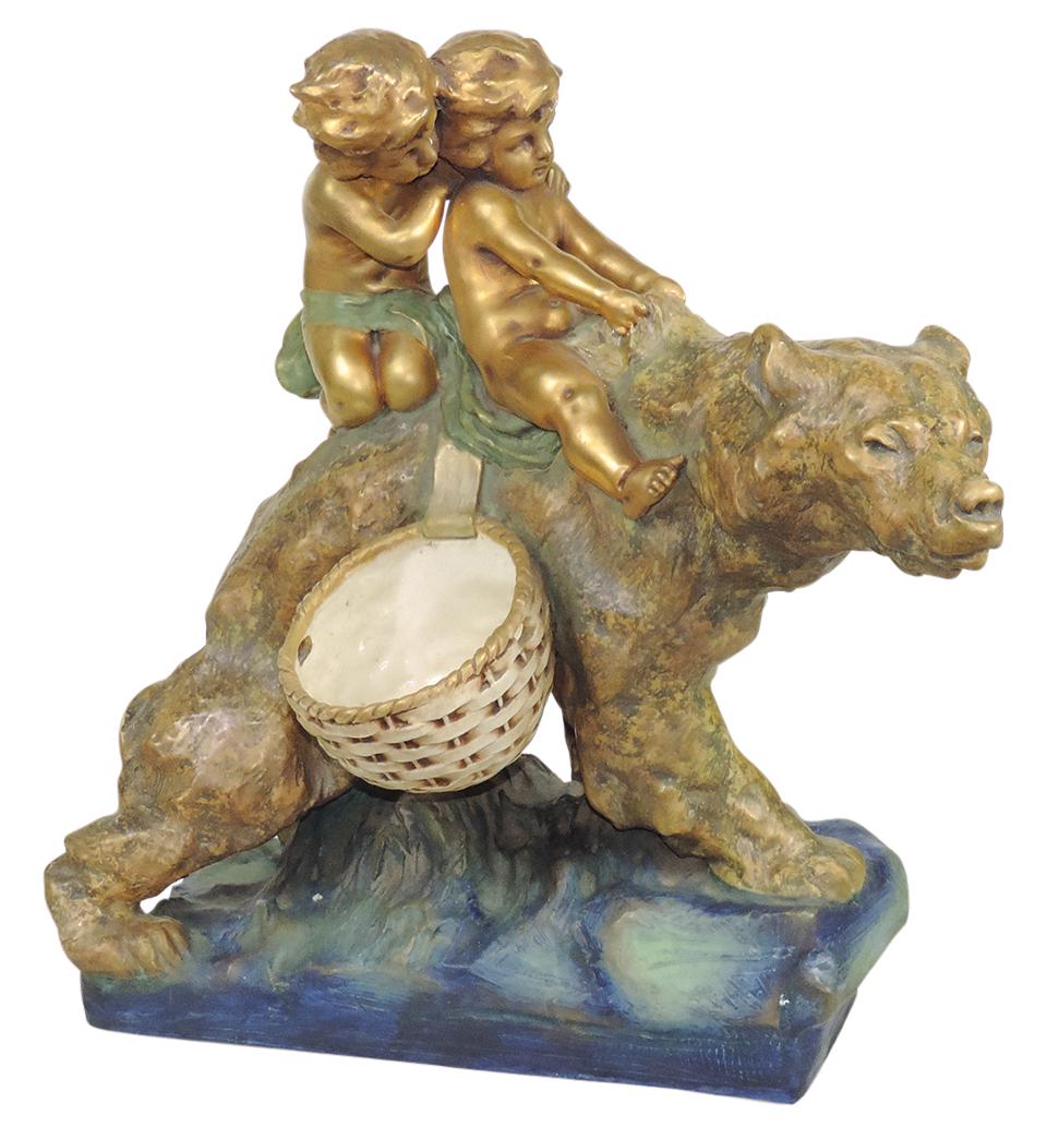 Porcelain, Putti Riding A Bear, Amphora Riessner & Kessel Turn-Teplitz hand-painted & gilt, incised: Porcelain, Putti Riding A Bear, Amphora Riessner & Kessel Turn-Teplitz hand-painted & gilt, incised marks, Good+ cond noting repair to ribbon at verso, 19.5"H x 18"W.