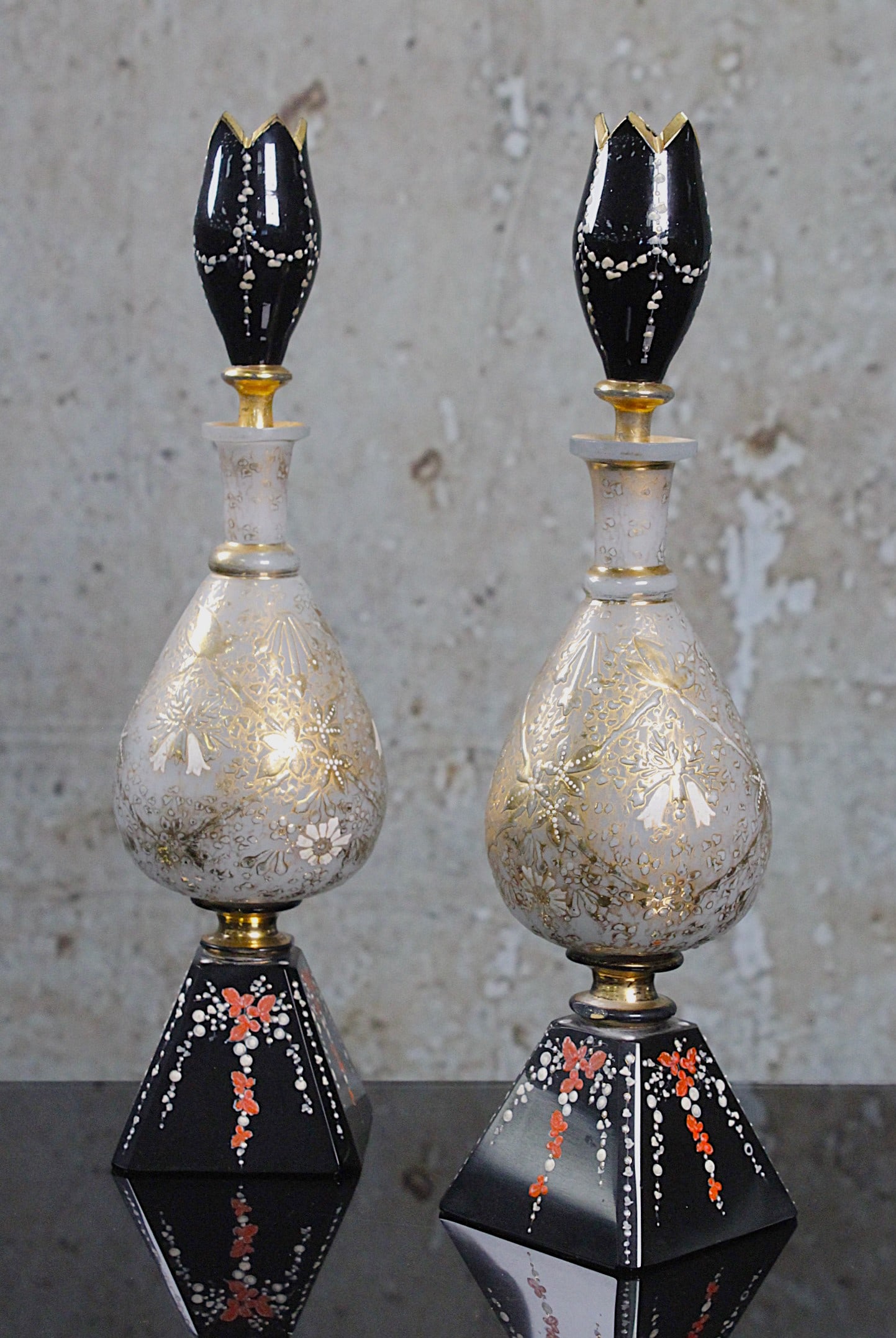 A Pair Of Aesthetic Opaline Art Glass Bottle Vases: French or Russian c.1875 with gilt enameled florals raised on pyramidal polished black glass vase under black lily form stoppers, Exc cond w/ some rubbing to gilt 12.25"H.