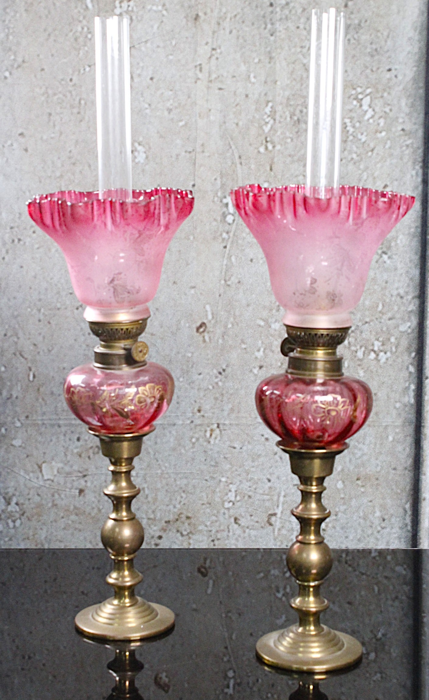 A Pair Of French Cranberry Glass Peg Lamps: 19th century with optic ribs, gilt florals set in bronze candlestands with associated etched rubina lily shades (inverted) Vg cond noting a chip on one shade fitter rim, 20"H. Incl chimney.