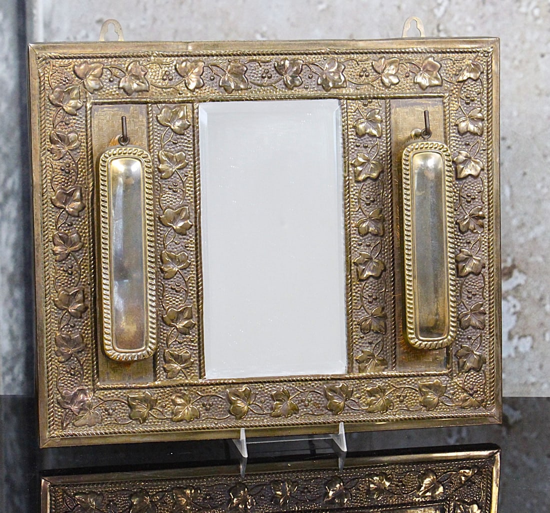 A Victorian Brass Repousse Hatters Mirror: 19th century with scroll vine boarder, beveled mirror and two brushes, VG cond, 13"H x 15"W.