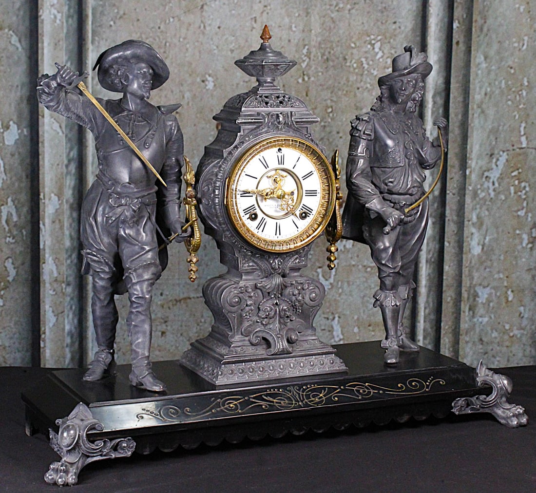 A Spectacular Ansonia Double Figure Mantle Clock: Late 19th century Don Caesar & Don Juan with exposed sunken escapement and porcelain chapter ring in Rococo white metal case flanked by standing figures with gilt sword blades surmounting an enameled