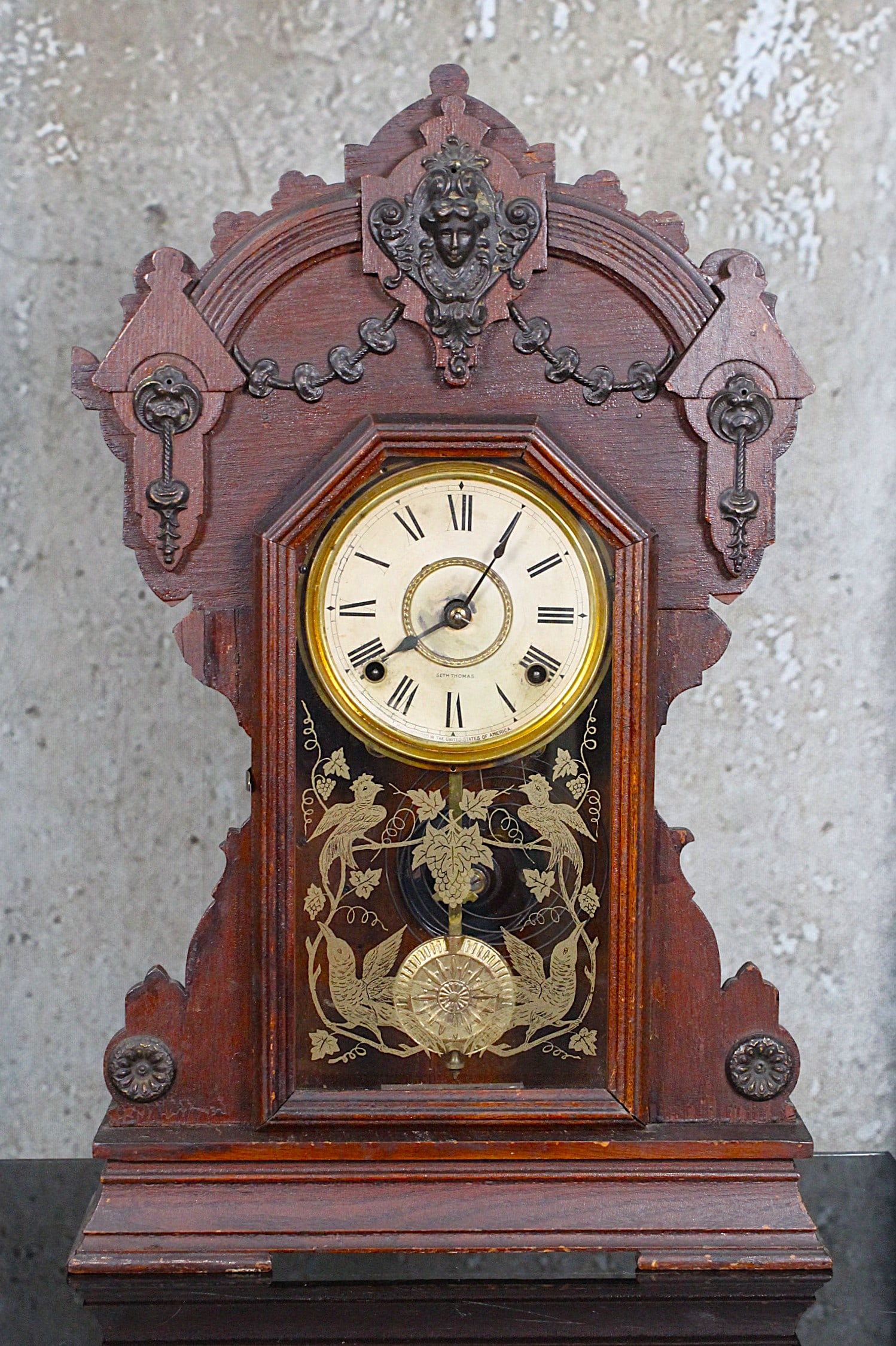 A Victorian Oak Shelf Clock By Seth Thomas: Late 19th century with embossed metal mounts incl. facial mask, VG original finish, reverse painted glass and working, 23"H