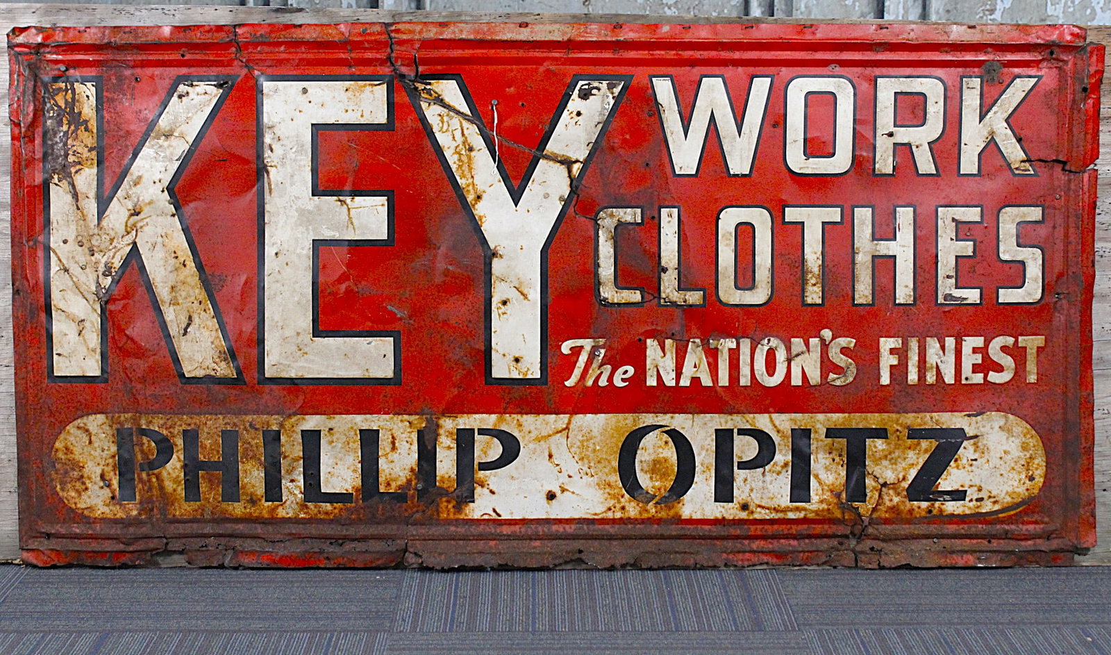 A Large Key Work Clothes Advertising Sign: Embossed tin litho in crusty cond with damage. Later mounted to plywood, 36"H x 69"W.