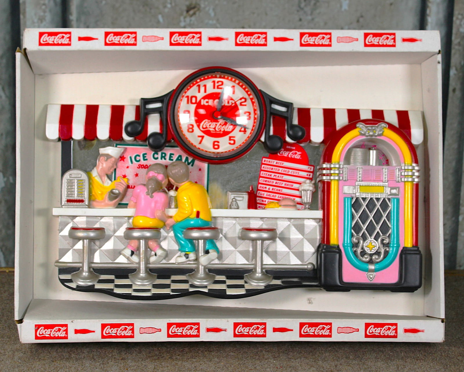 A Coca-Cola Nostalgic Soda Fountain Wall Clock: C.1990 Molded plastic w/quartz movement unused and mint in original box, 17"H x 23"W overall
