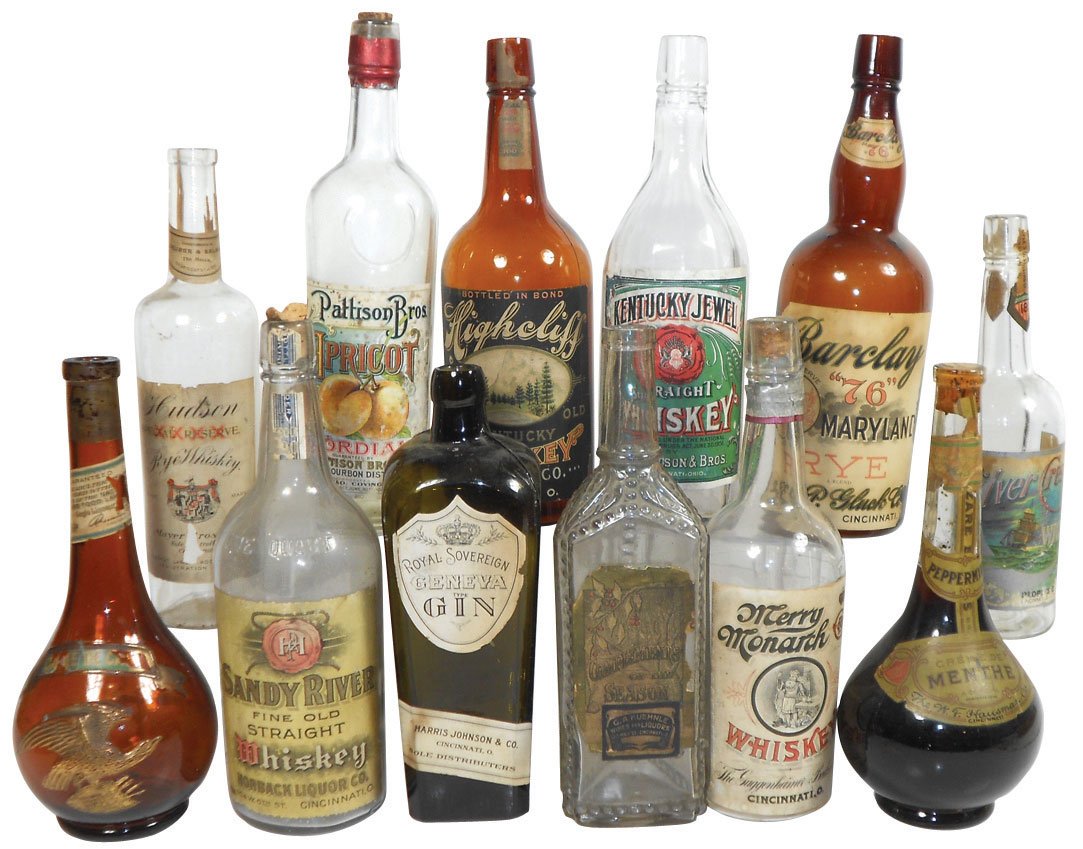 Back bar whiskey bottles (12), cork tops, various Cinci: Back bar whiskey bottles (12), cork tops, various Cincinnati distilleries, assorted shapes, some embossed, one w/eagle & mfgr shield, bottles Exc cond, orig paper labels Good to VG cond, 10"-12"H.