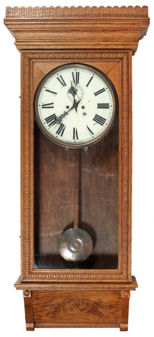 Wall clock, Waterbury Clock Co., ornate oak cabinet,: Wall clock, Waterbury Clock Co., ornate oak cabinet, Roman numerals on painted metal face w/second hand dial, key wind, orig maker's tag inside case, brass pendulum & key, Exc cond, 51"H x 21.5"W x 8"