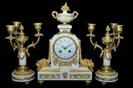 CLOCK AND CANDELABRA SET: Circa 1890, base made of white marble decorated with gilded patina in the shapes of abundance horns, ribbons and plantation. Enamel numerals decorated with roses. Mechanism manufactured by JAPY. (this