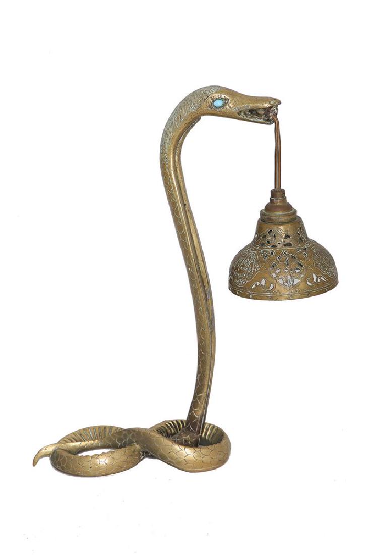AN ISLAMIC BRASS SNAKE LAMP: The coiled snake holding the dome form shade in its mouth 32 cm high