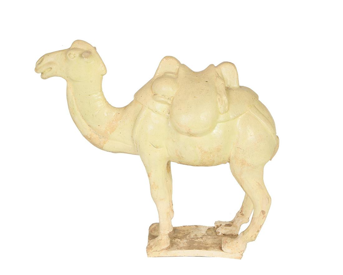 A TANG DYNASTY CHINESE TOMB MODEL OF A CAMEL: Pale pottery modelled with an animal standing square on a rectangular base, rounded saddlebags slung between its humps to which are also hung flasks and pelts, the camel facing forwards with ears atte