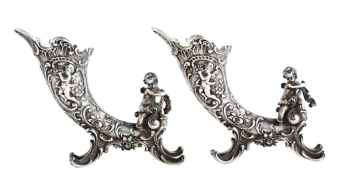 GEBRUDER GLASER. PAIR OF SILVER CORNUCOPIAS: Circa 1890. Neo-rococo style. Rich relief decorations with interlaced lines, incorporating flowers and putti; each terminated with a putto holding a flower garland. Signed. Total weight: approx. 434.7